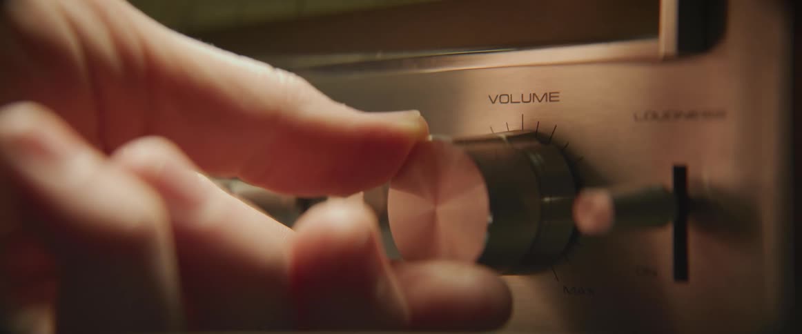 Person turns the volume knob on a vintage stereo inside a dimly lit room