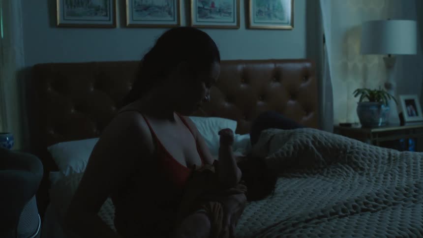 A woman sits on the corner of a bed and tries to comfort a baby