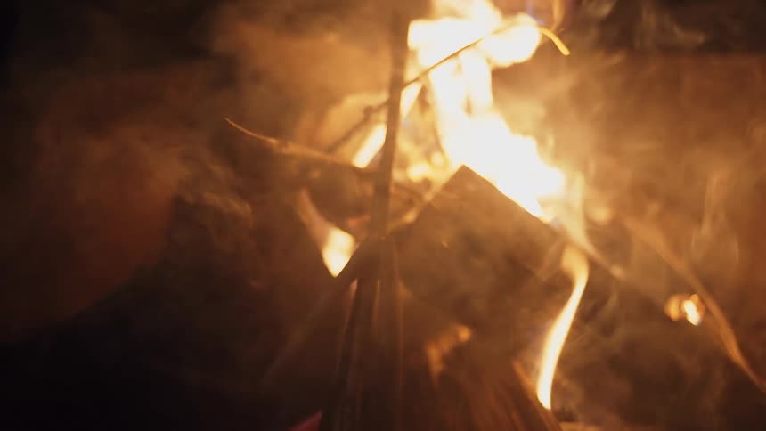 A campfire burns outdoors at night