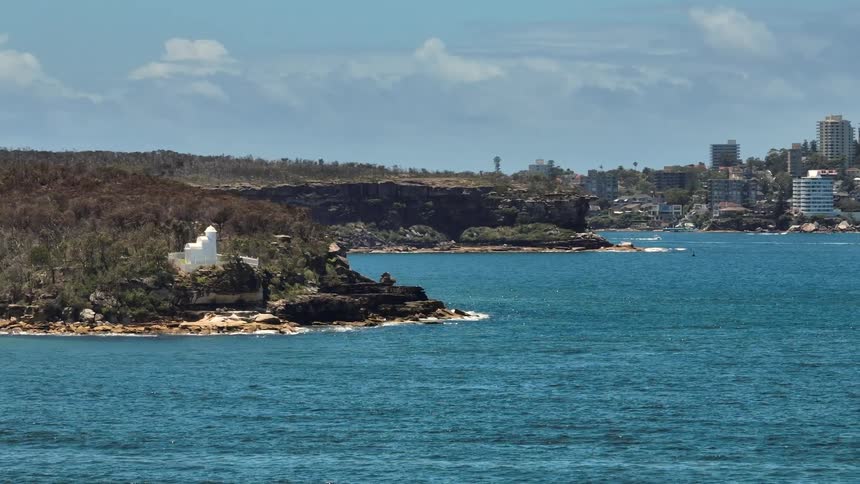 Aerial view of a white isolated building close to the ocean near the city skyline