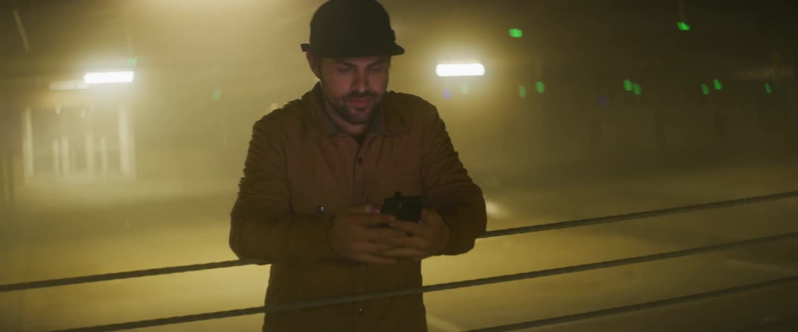 A man rests his arms on safety railing while using his smartphone in a parking garage
