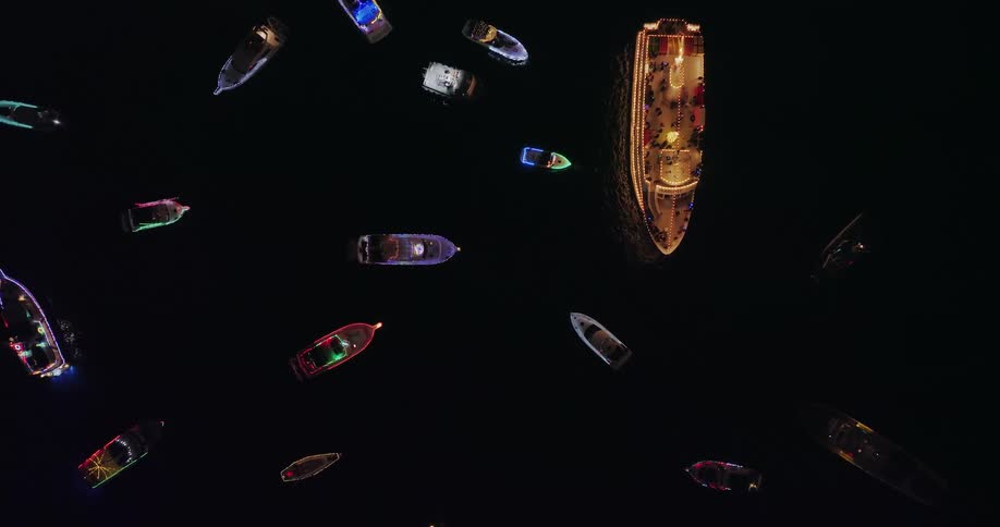 Top down twist over lit up boats on the water at night