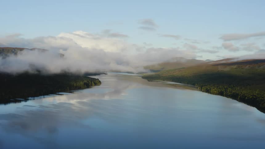 An almost completely still body of water is reflecting the low clouds in the sky
