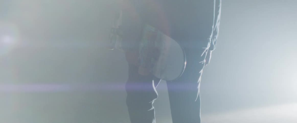 A person is walking in the fog carrying a skateboard