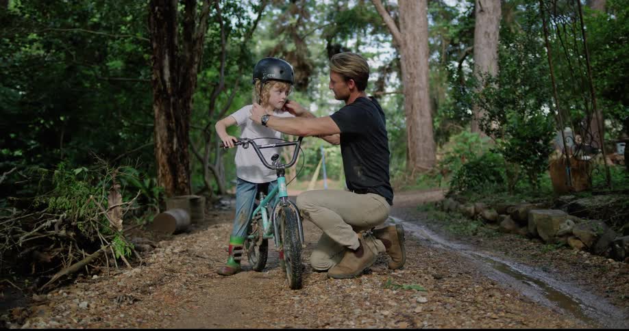 Father putting a bike helmet on his son on  a dirt road in an outdoor area