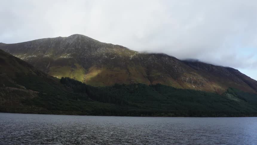 A mountain on the moving water under a cloudy sky