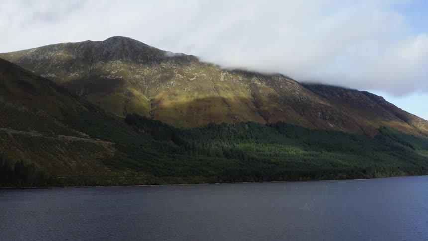 Aerial view of a clouds hanging over a mountain close to a lake in the morning