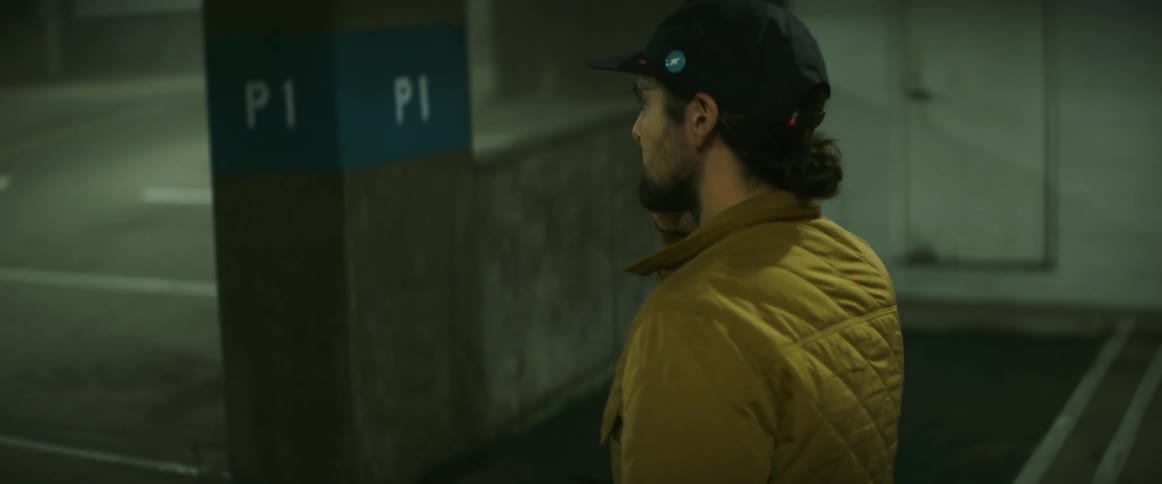 A man holds his smartphone to his ear while walking through a parking garage