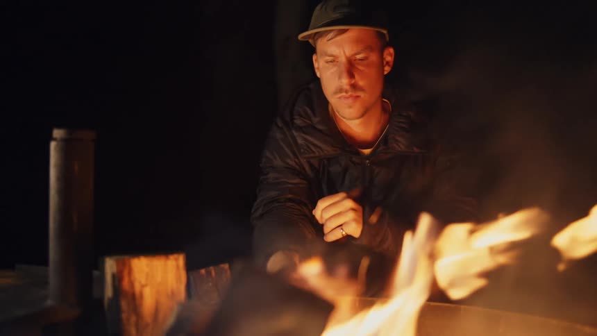 A man sits by the campfire at night