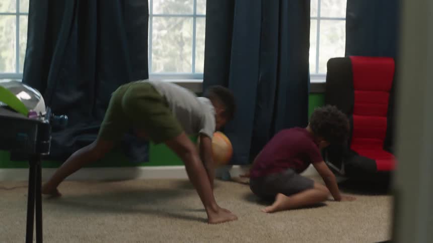 Two young boys play with a basketball indoors while bouncing it off the wall and chasing it around