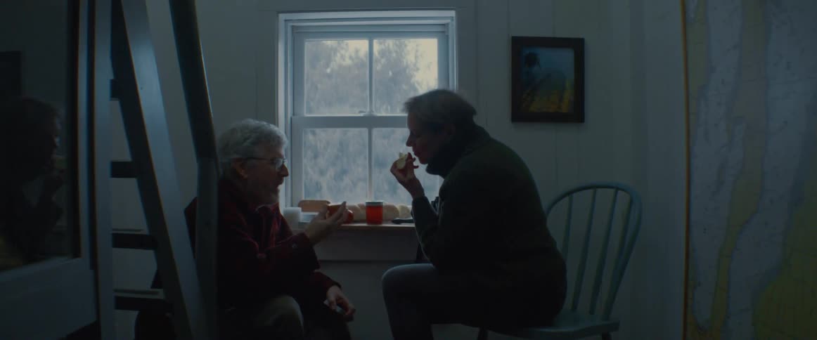 Two people sit at a window sill eating a small meal or snack together