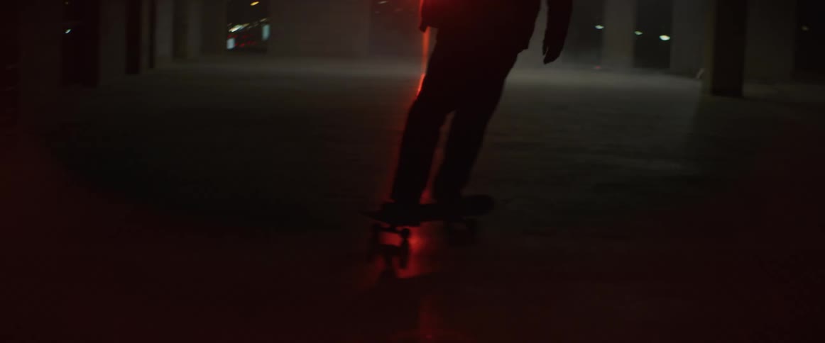 A person rides a skateboard through a dimly lit and empty floor of a building at night