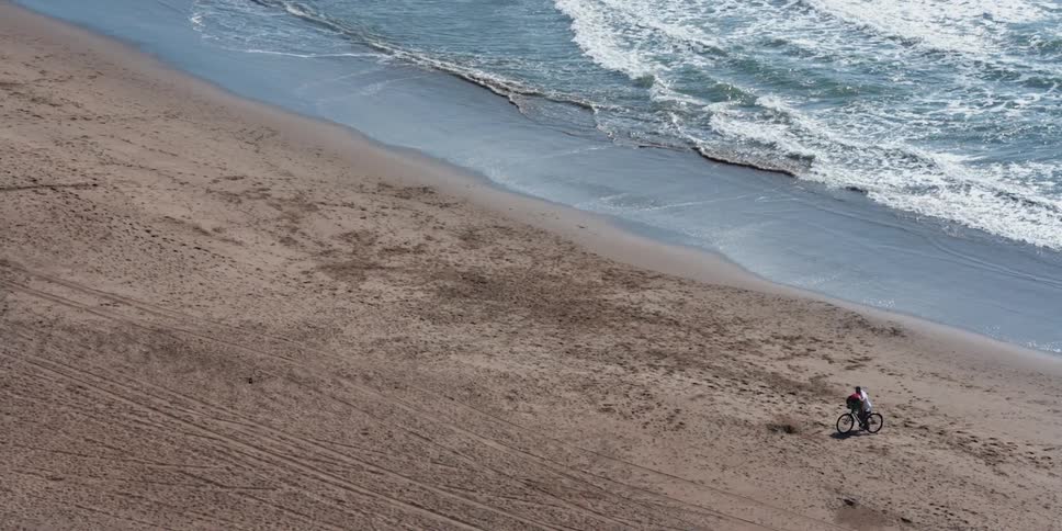 A cyclist pushes a bicycle across a beach during the day