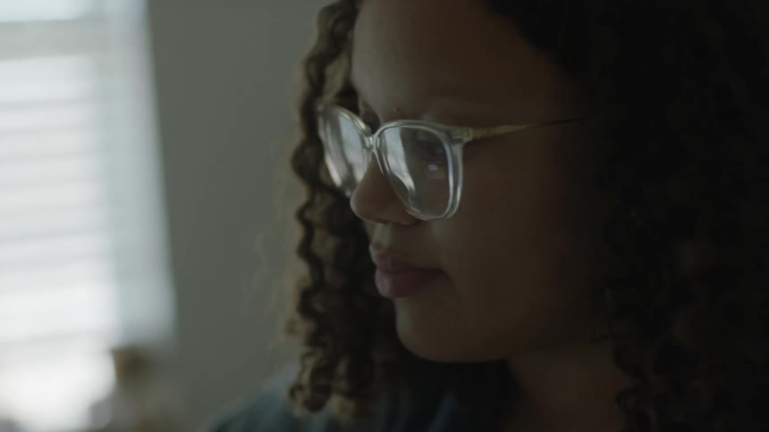 A young woman with curly hair and glasses concentrates while looking at a computer display