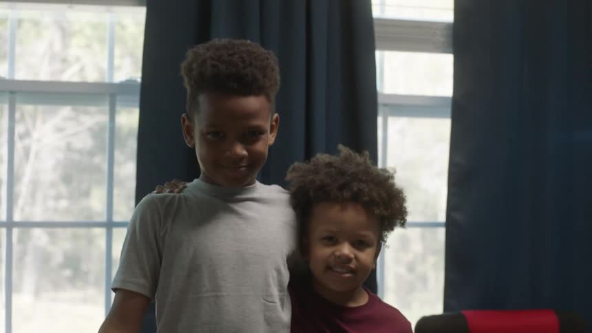 Two young brothers posing for a portrait indoors in front of windows