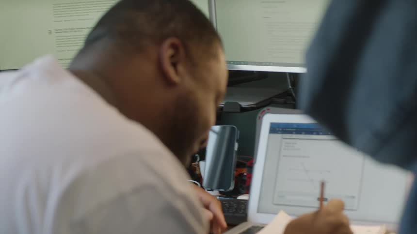 A man takes notes while looking at a graph on his laptop