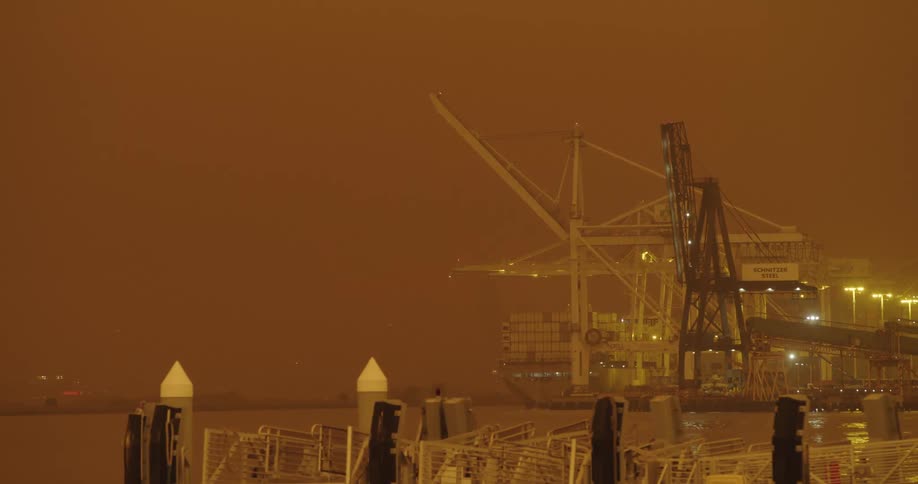 A ship and cranes along a dock under an orange sky