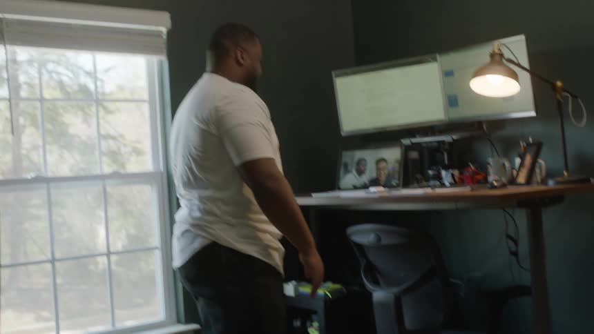 A man puts his son down letting him leave the room as he goes back to his meeting at a standing desk