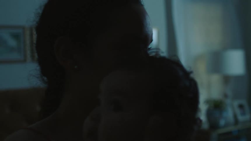 A woman rocks a baby in her arms in a dimly lit bedroom