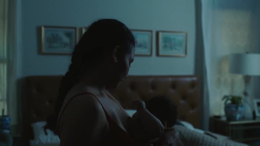 Woman rocks baby while standing next to bed with her sleeping spouse