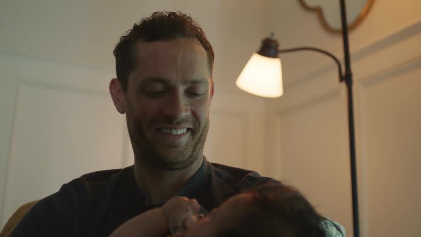 A man smiles as he looks down at the baby hes holding