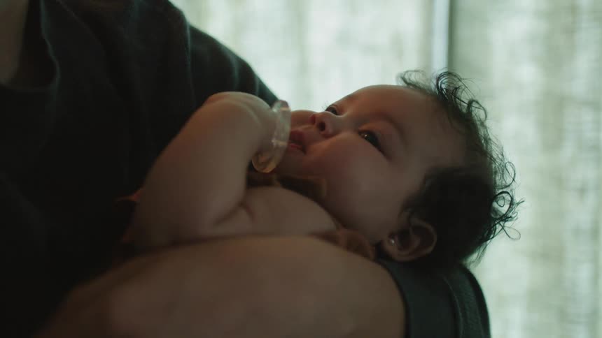 Adult holds a baby playing with a pacifier in their arms ands rocks the child gently