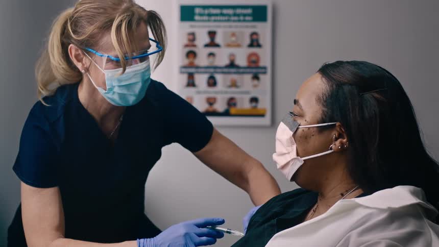 White nurse wearing vaccinating a black woman for coronavirus