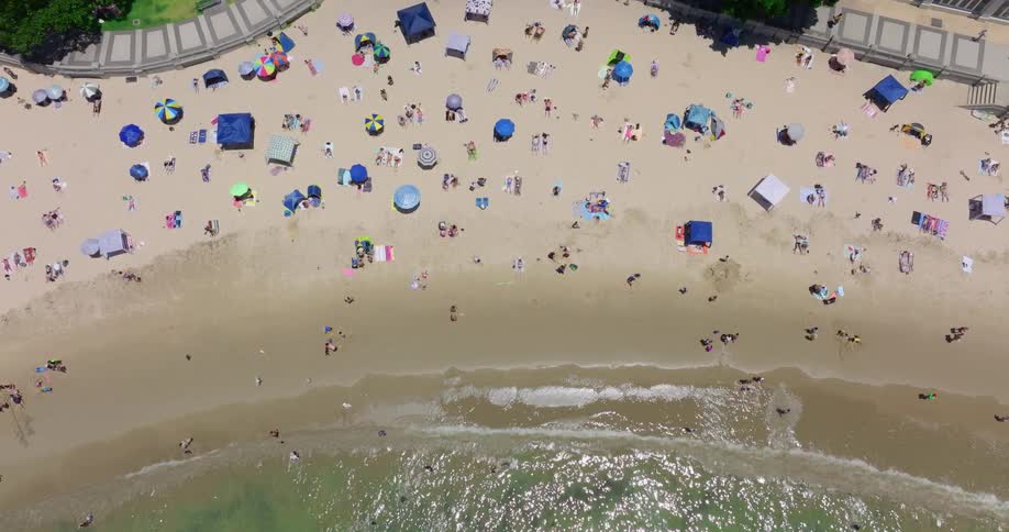 People sunbathe on the beach and wade in the ocean