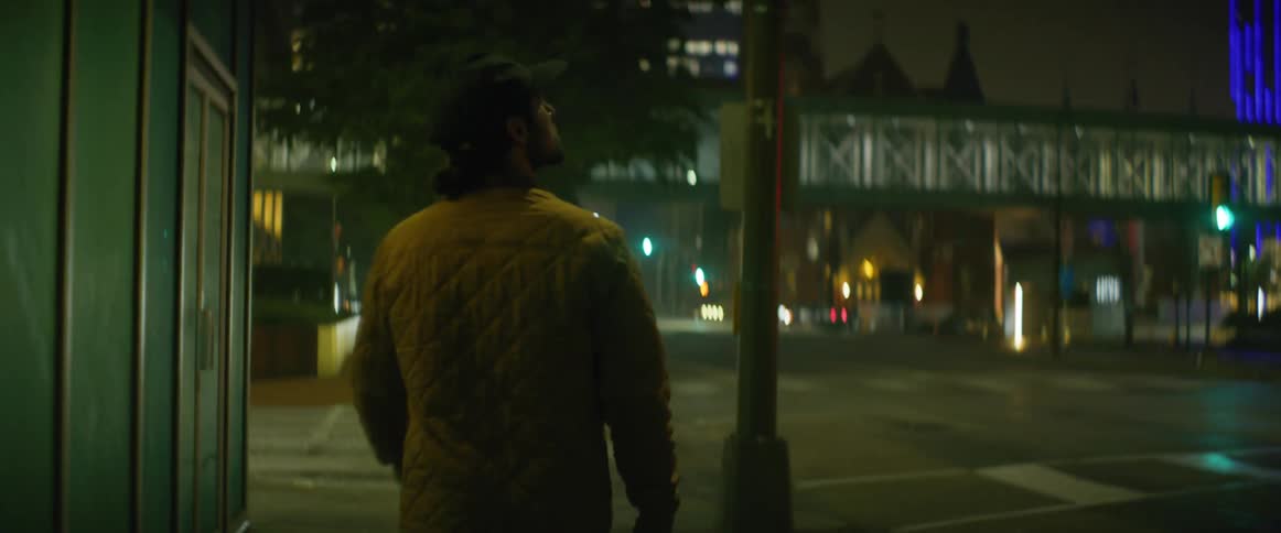 Man wearing a baseball hat and a jacket walking on the city street at night