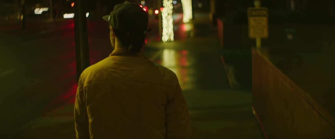 A man walks down a city sidewalk bright christmas lights on street posts at night