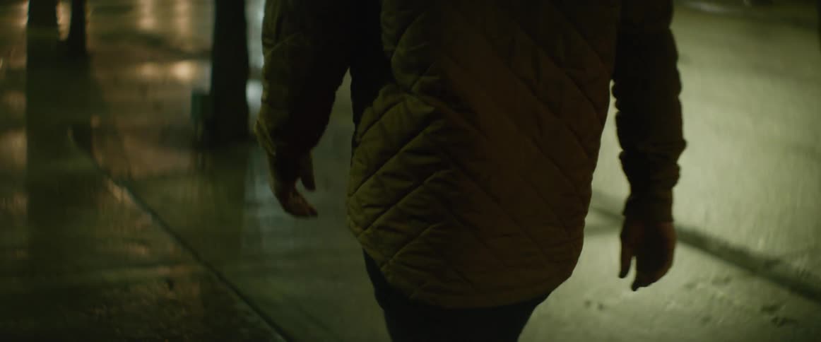 A man walks along a sidewalk beside a road in a city at night