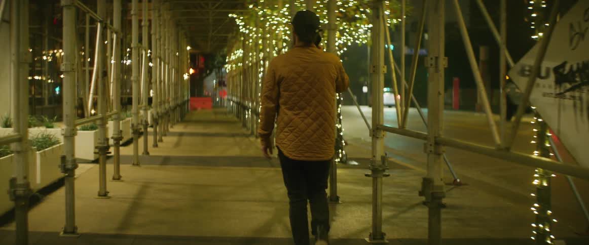 Man holds phone to his ear as he walks under enclosure decorated by christmas lights as traffic moves down street