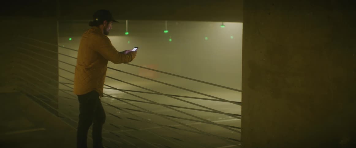 A man uses his smartphone while leaning against railing in a parking garage