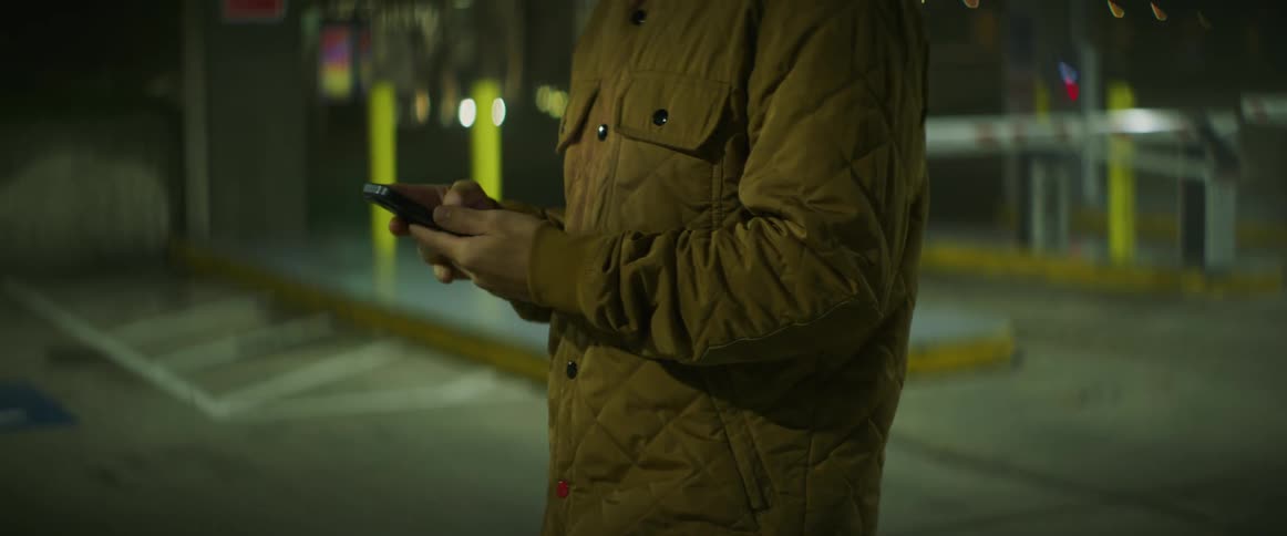 White man standing alone and using his smartphone in the middle of a parking lot