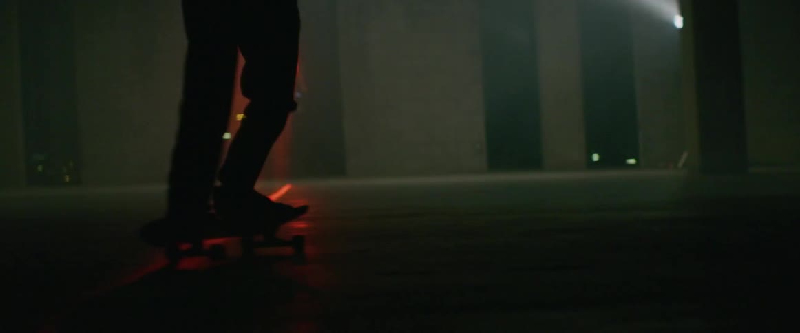 Person rides skateboard through red laser light as gaps in wall show city lights