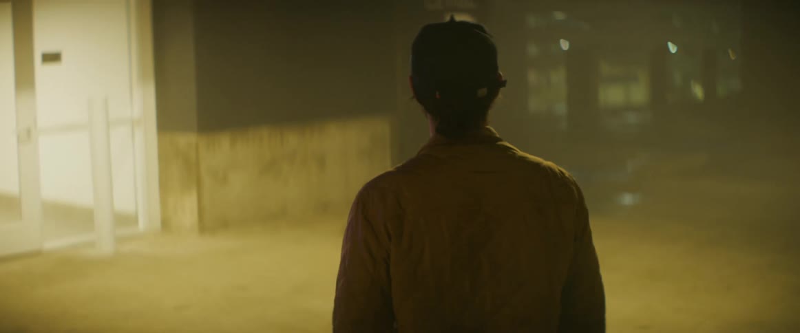 Man wearing a baseball cap walking inside a parking garage at night