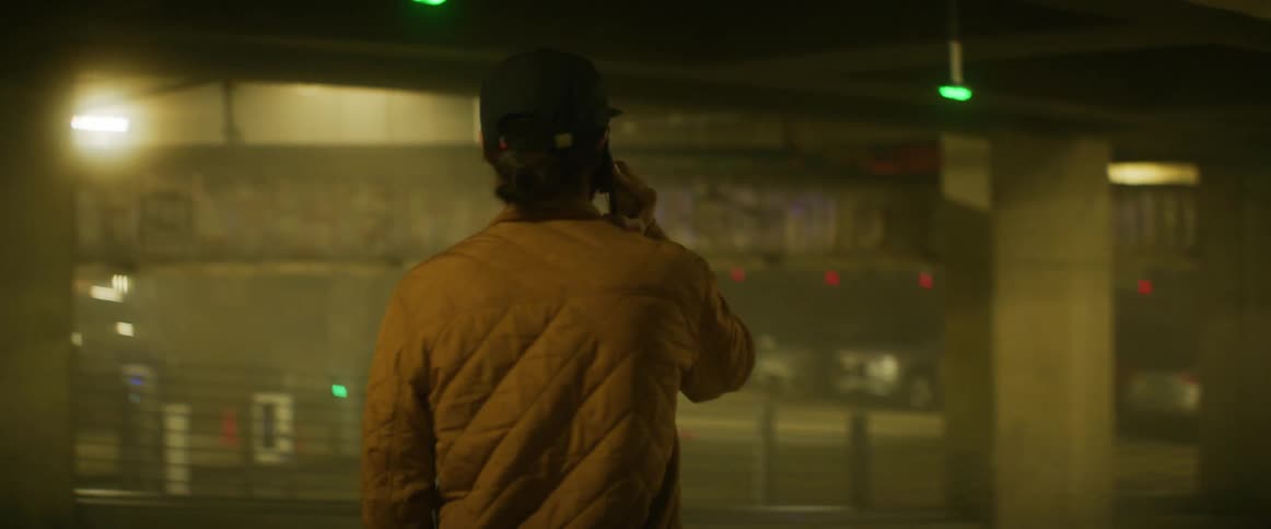 A man talks on his phone while standing in a parking garage