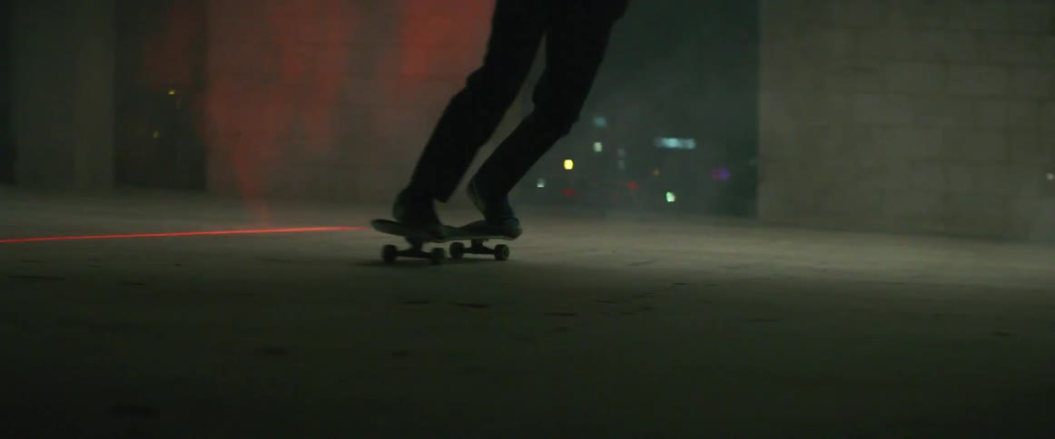 Skateboarder rides board across concrete past red laser lighting