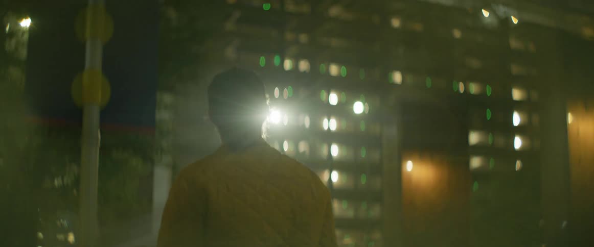 A man walking down a city street at night points up at a building