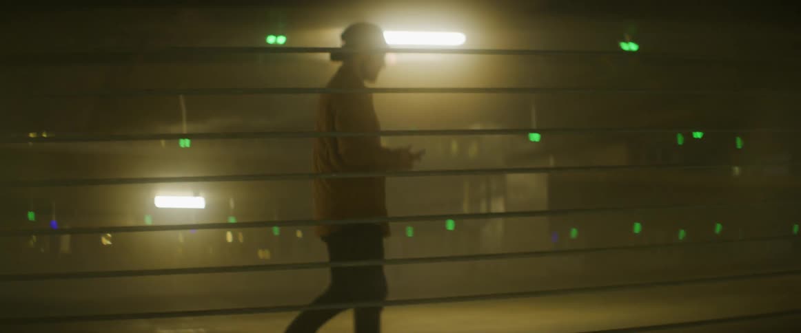Man wearing a baseball hat and a jacket uses a smartphone inside a foggy parking garage