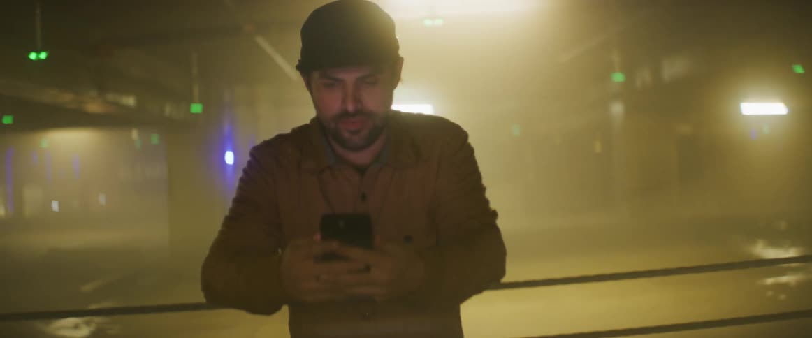 A man checks his smartphone while leaning against the railing in a public parking garage