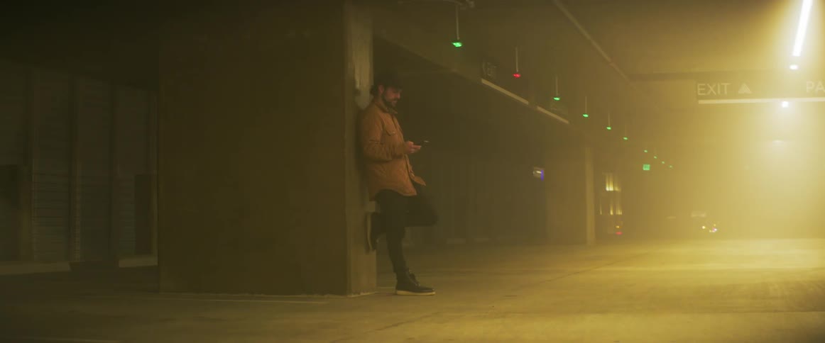 A man is leaning against a wall looking at his cellphone