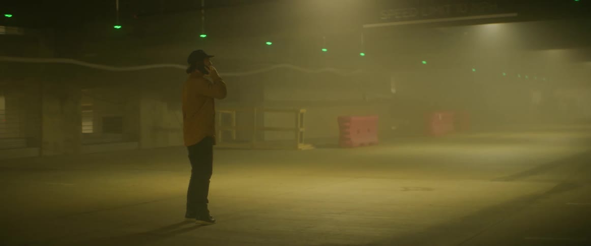 A man is walking through a smoke filled parking garage while talking on his phone