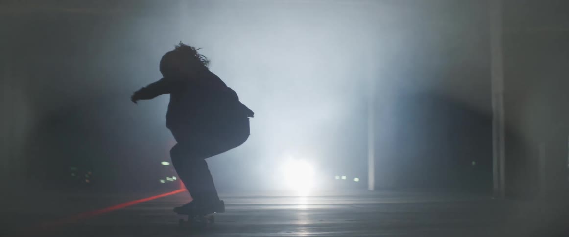 Person rides skateboard in dim area near laser as they are cast into silhouette by spotlight