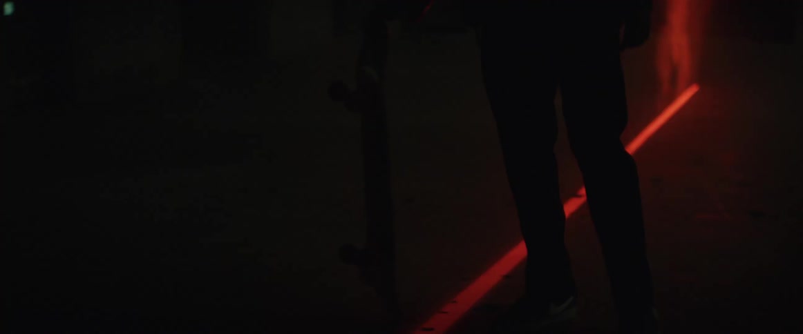 Skateboarder stands spinning skateboard on one end next to laser light line