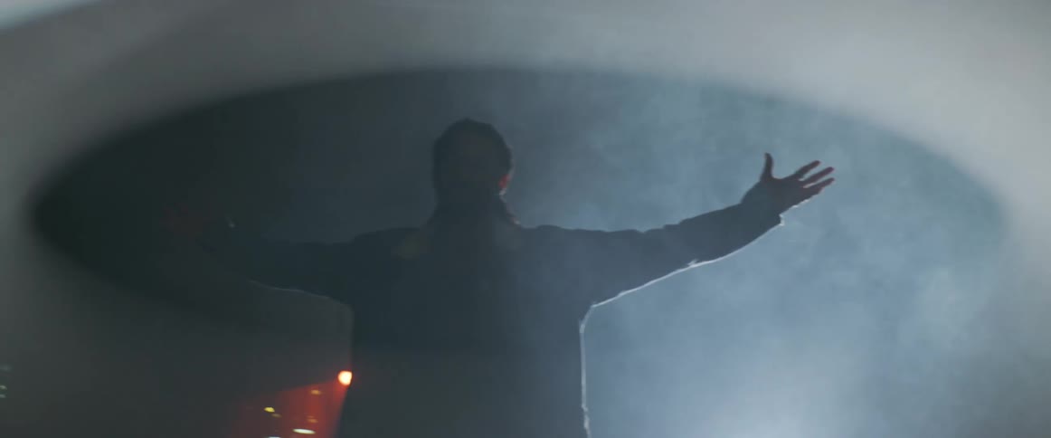 Silhouette of a man with open arms in front of a light surrounded by white smoke at night