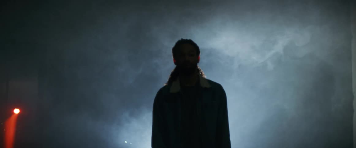 A man spins his skateboard against the ground while standing in a smoke filled tunnel