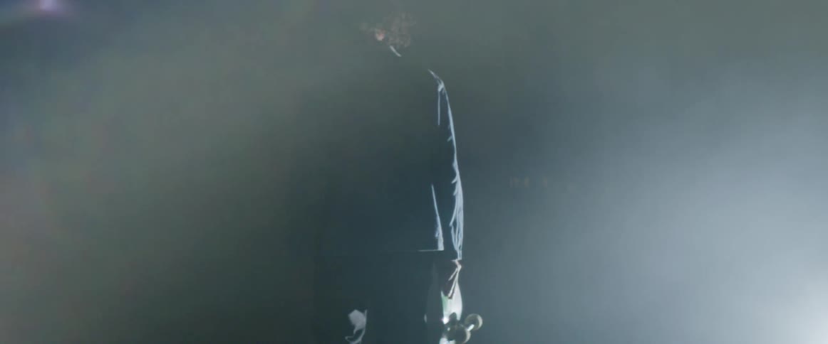Man carrying a skateboard on a hand walking inside a building filled with white smoke