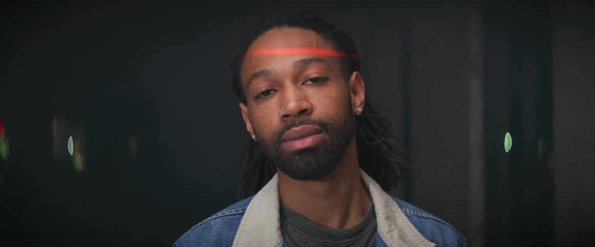 A red laser scans up and down a mans face while he poses in a room