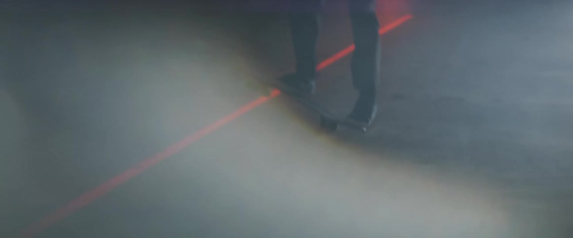 A young man skateboards at night as cars drive past